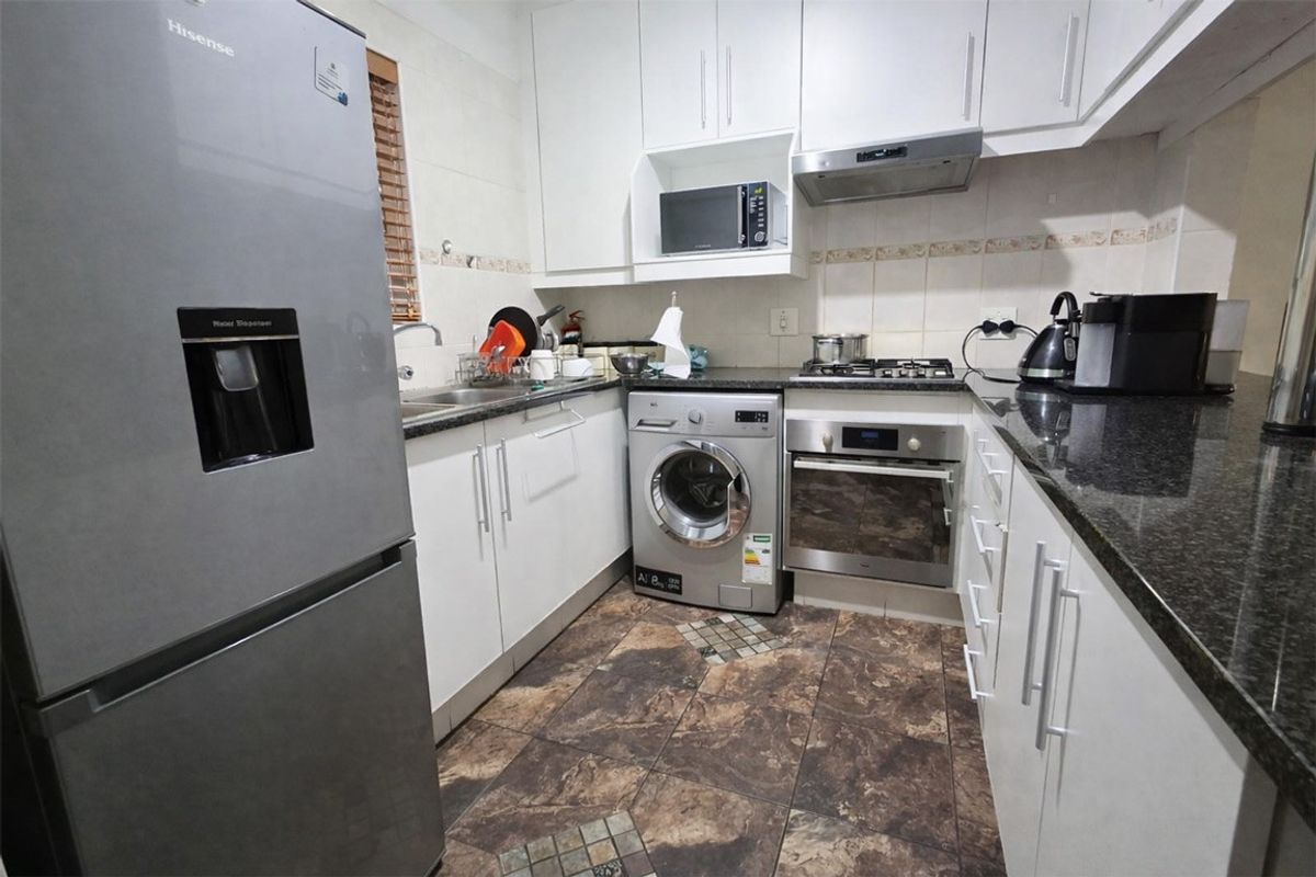 Compact kitchen featuring granite countertops, built-in oven, gas hob, extractor fan, and ample white cabinetry with tiled flooring.