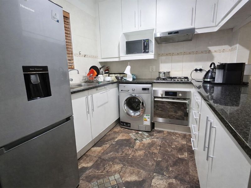 Compact kitchen featuring granite countertops, built-in oven, gas hob, extractor fan, and ample white cabinetry with tiled flooring.