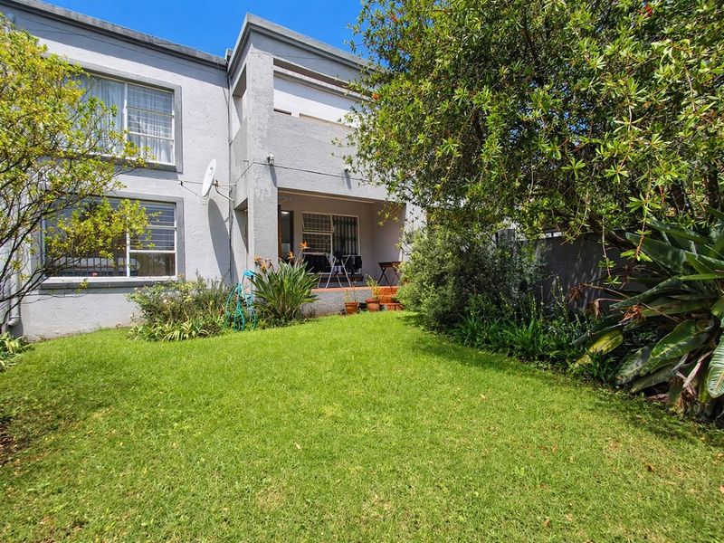 Rear view of the apartment building featuring a covered patio area, established garden, and security-fitted windows.