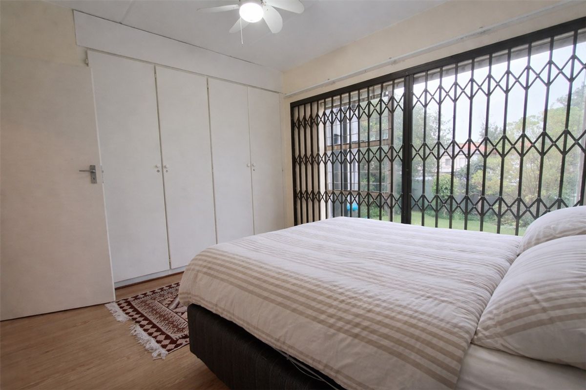 A bedroom featuring built-in cupboards, laminate flooring, a ceiling fan, and a security gate over the window.