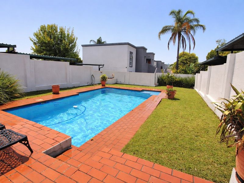 Private outdoor swimming pool area featuring brick paving, a well-maintained lawn, and secure boundary walls.