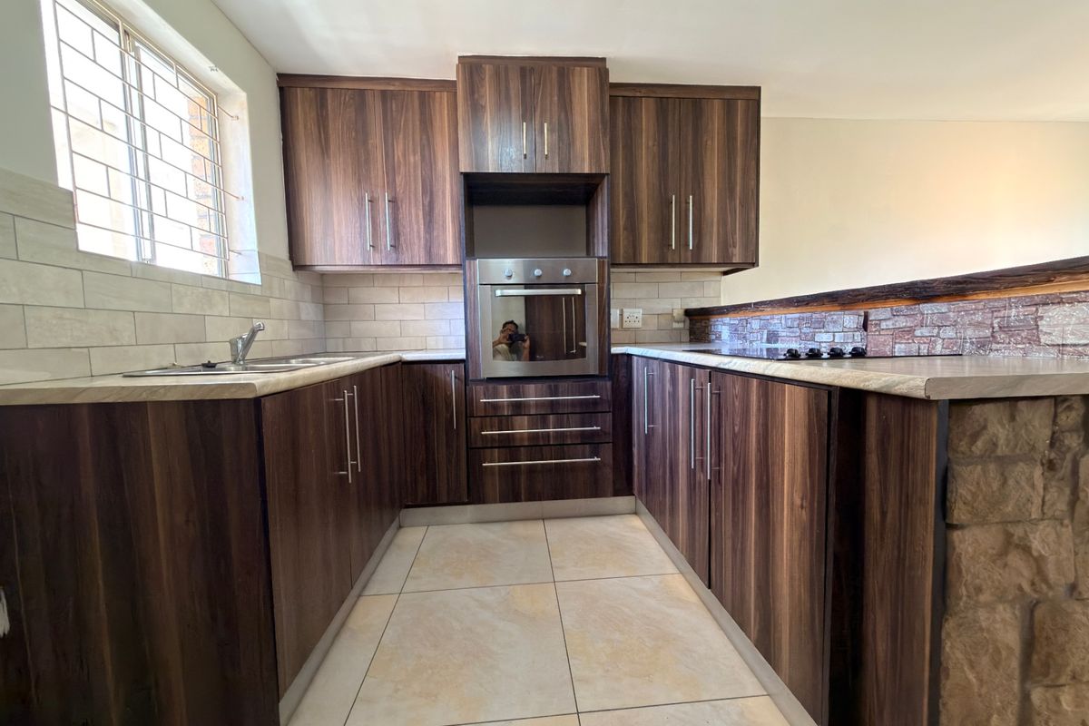 Modern kitchen featuring dark wood-grain cabinetry, built-in oven, hob, tiled backsplash, and neutral floor tiles, offering a clean and functional workspace.