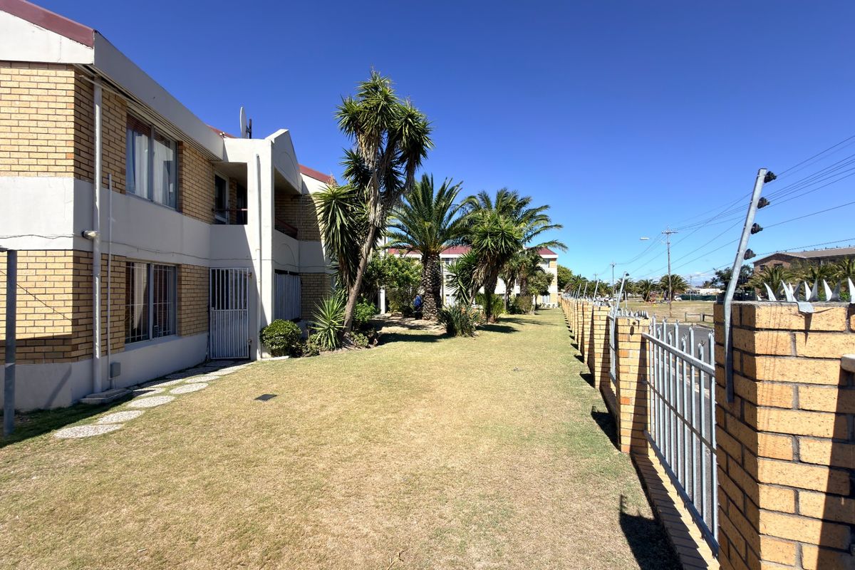A view of the apartment building's rear exterior, featuring a well-maintained lawn, brick facade, and secure perimeter fencing.