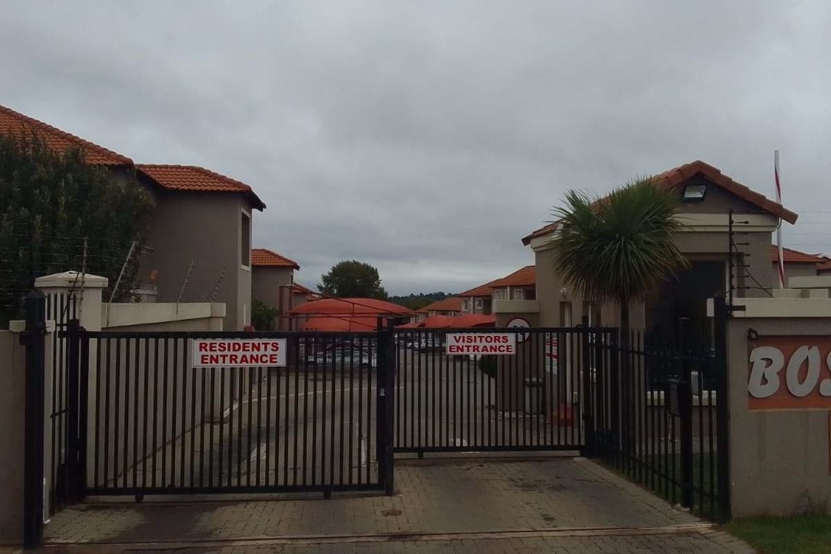 The main entrance to the residential complex featuring a secure gated access point with separate lanes for residents and visitors.