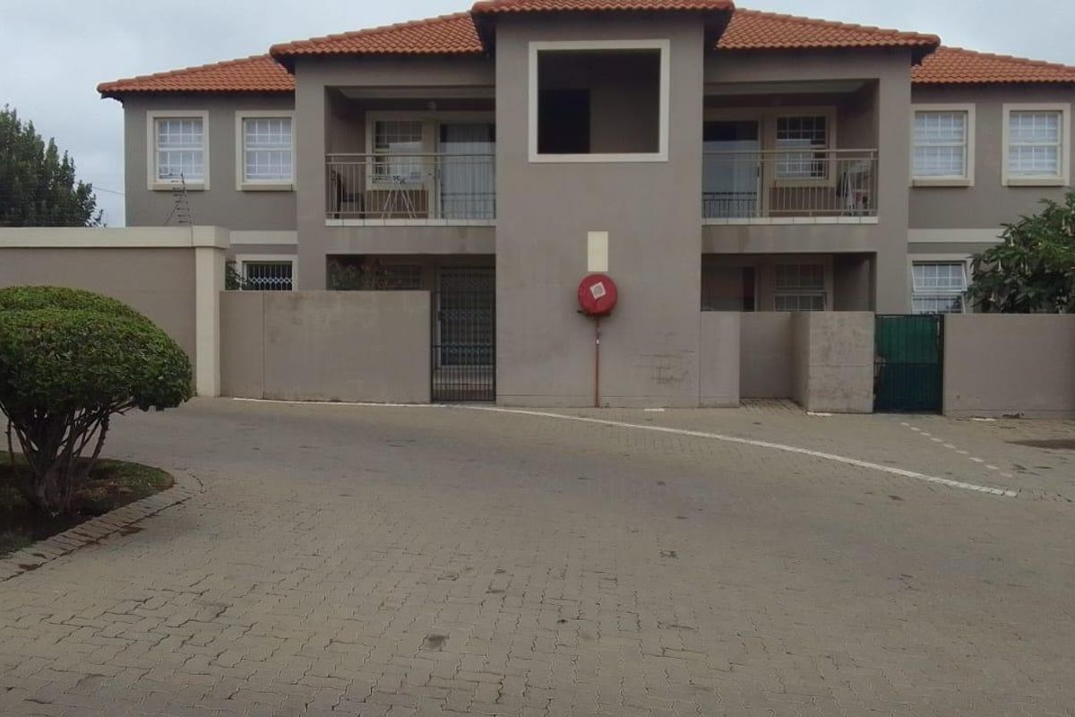 Front elevation of a two-story townhouse complex featuring a paved driveway, balconies with metal railings, and a tiled roof.