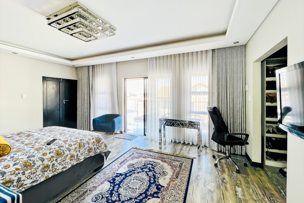 Spacious bedroom featuring recessed ceiling lighting, a crystal chandelier, laminate flooring, and direct access to a private balcony through sliding glass doors.