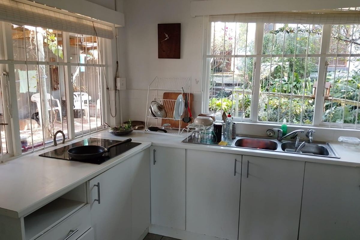 A functional kitchen featuring white cabinetry, laminate countertops, a stainless steel double sink, and an integrated induction hob with views of the garden.