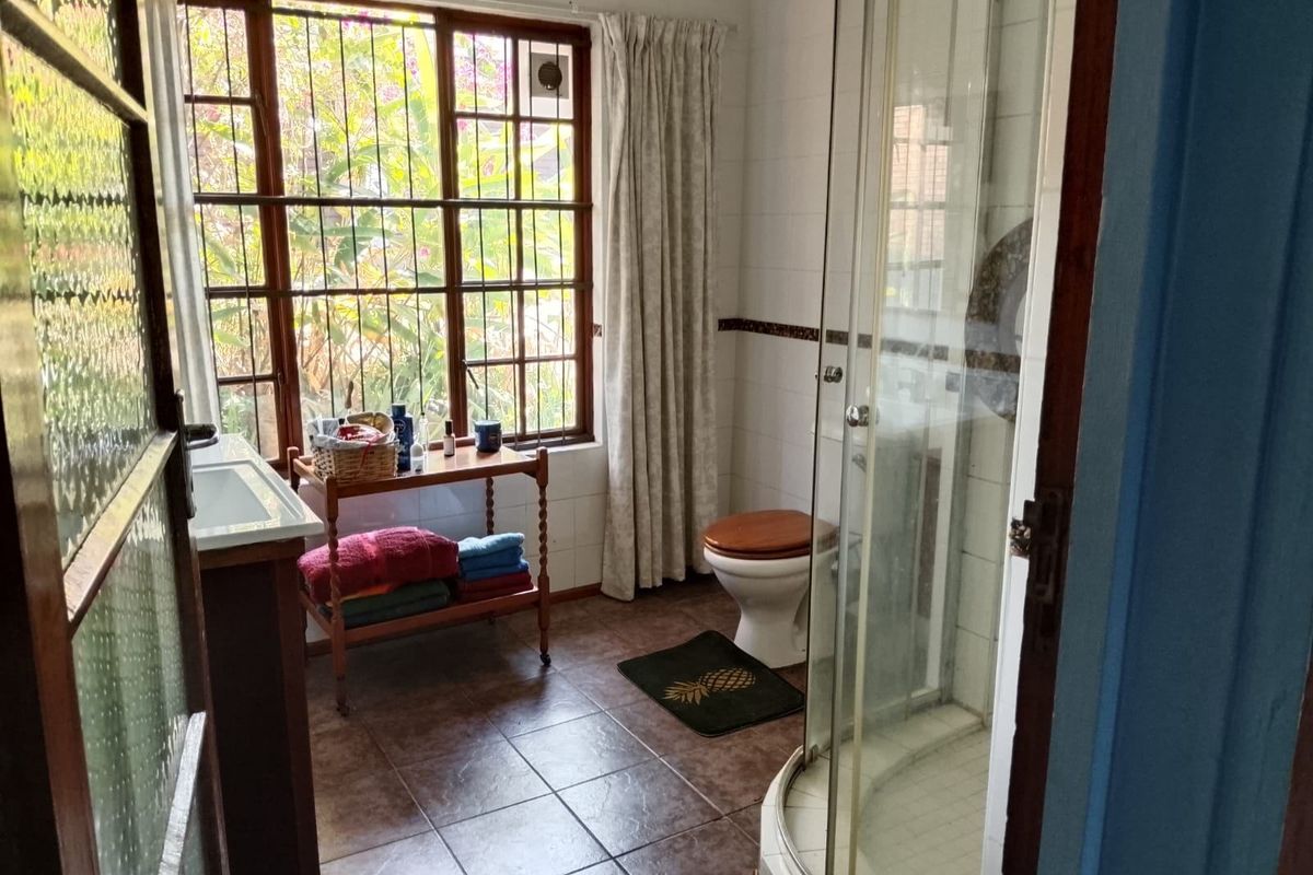 A functional bathroom featuring a corner shower enclosure, toilet, and vanity basin with tiled flooring and natural light from a large window.