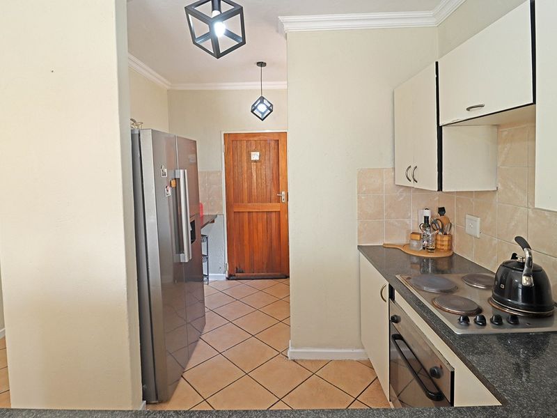 A functional kitchen featuring built-in cabinetry, granite countertops, an electric hob, and an oven, with tiled flooring and direct access to an exterior door.