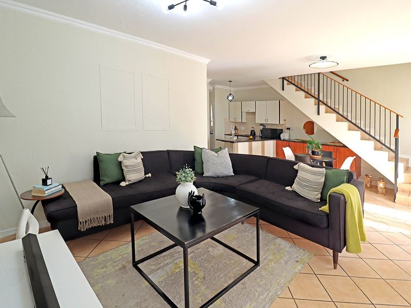 Open-plan living area featuring tiled flooring, a staircase with a metal balustrade, and an integrated kitchen space.
