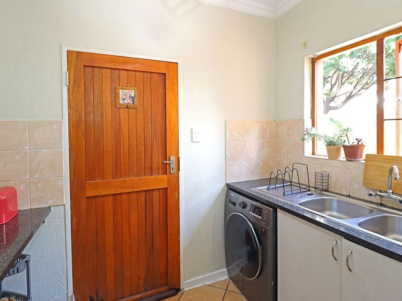 Functional laundry area featuring a double stainless steel sink, granite countertops, tiled splashback, and built-in cabinetry with direct access to an exterior door.