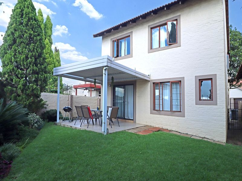 Rear view of the property featuring a covered patio, landscaped garden, and secure perimeter wall with electric fencing.
