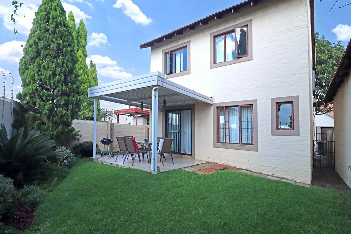 Rear view of the property featuring a covered patio, landscaped garden, and secure perimeter wall with electric fencing.