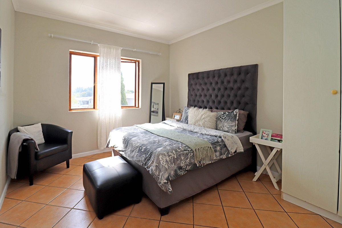 A well-lit bedroom featuring tiled flooring, built-in cupboards, and wooden window frames, offering a comfortable and functional living space.