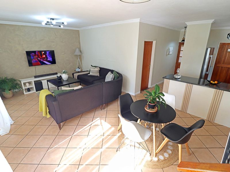 An open-plan living and dining area featuring tiled flooring, a breakfast counter with granite tops, and a textured feature wall.