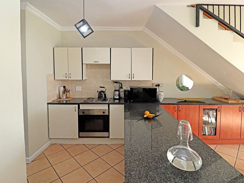 Compact kitchen featuring granite countertops, built-in oven and hob, and cabinetry, conveniently situated beneath the staircase.
