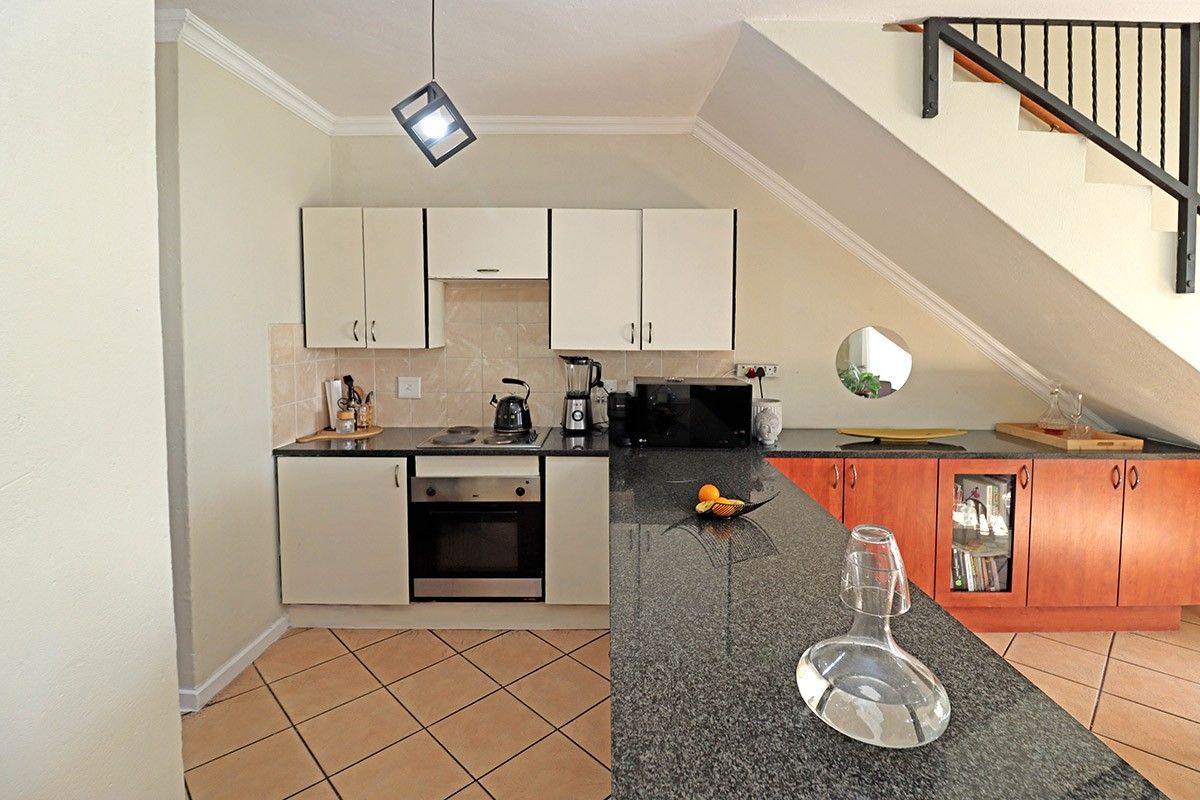 Compact kitchen featuring granite countertops, built-in oven and hob, and cabinetry, conveniently situated beneath the staircase.