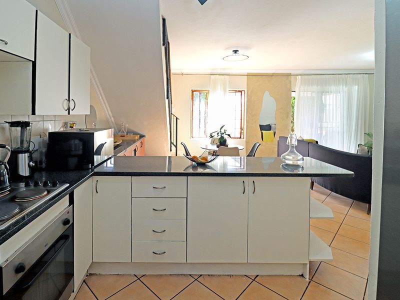 Open-plan kitchen and living area featuring built-in cabinetry, granite countertops, integrated oven and hob, and tiled flooring throughout.