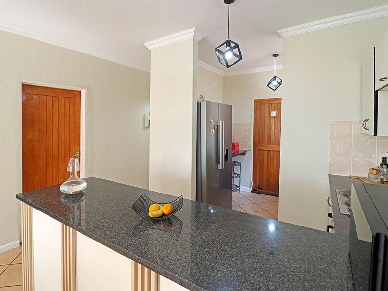A functional kitchen featuring a granite-topped breakfast bar, tiled backsplash, and modern pendant lighting, with direct access to adjacent rooms.