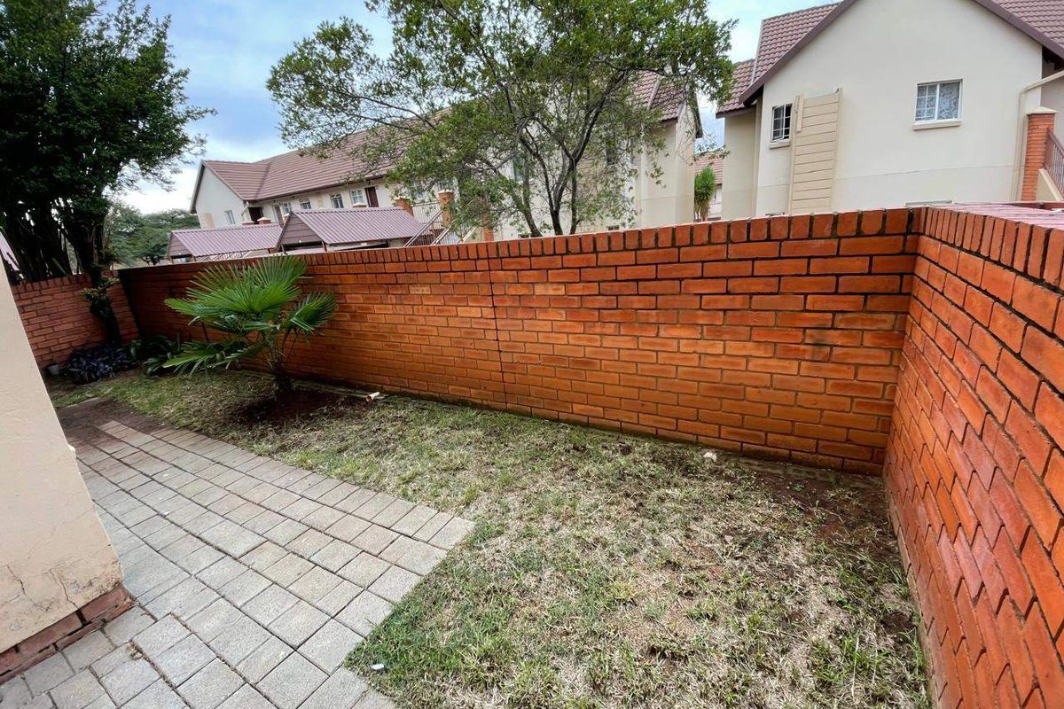 A private rear garden area featuring a brick boundary wall, a paved patio section, and a small lawn space.