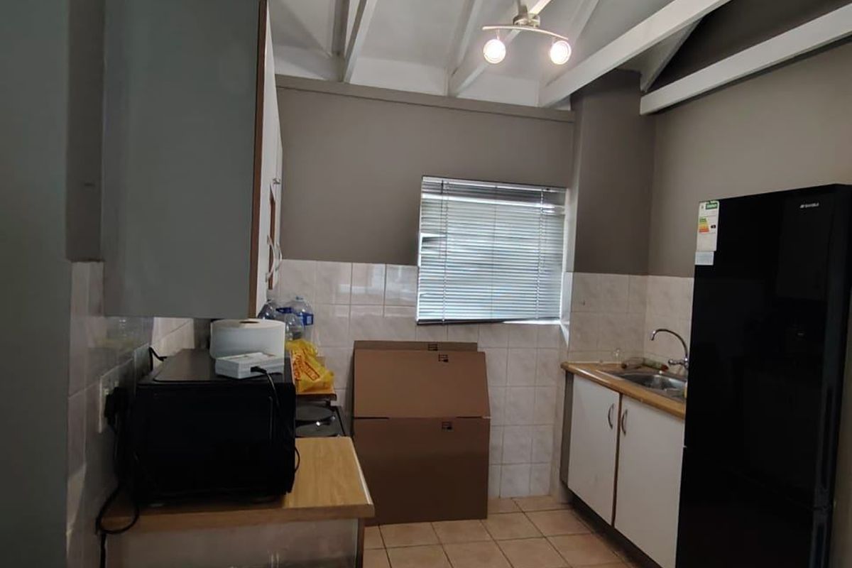 Compact kitchen featuring exposed rafters, tiled backsplash, laminate countertops, and functional cabinetry, offering a practical layout with potential for modern updates.