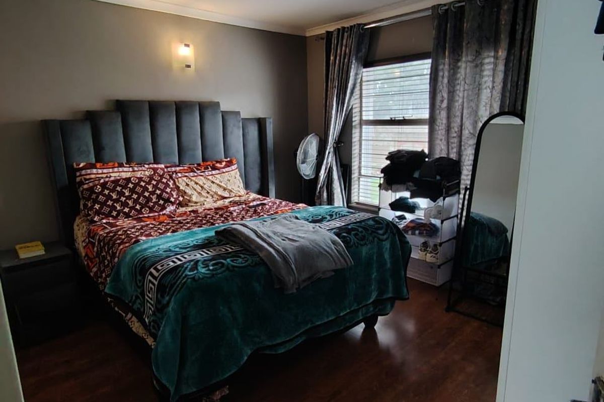 A well-proportioned bedroom featuring dark laminate flooring, neutral wall tones, and a window that provides natural light.