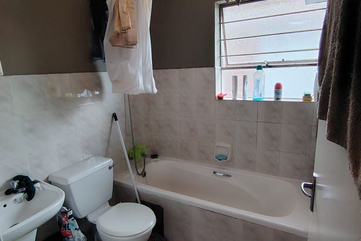 A functional bathroom featuring a bathtub, pedestal basin, and toilet with tiled finishes, requiring cosmetic updates to modernize the space.