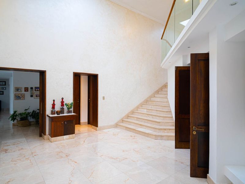 Spacious grand entrance hall featuring polished marble flooring, a sweeping stone staircase with a modern glass balustrade, and high ceilings.