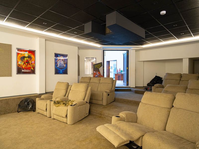 Dedicated home cinema room featuring tiered seating levels, acoustic ceiling tiles, and integrated projector housing for an immersive viewing experience.