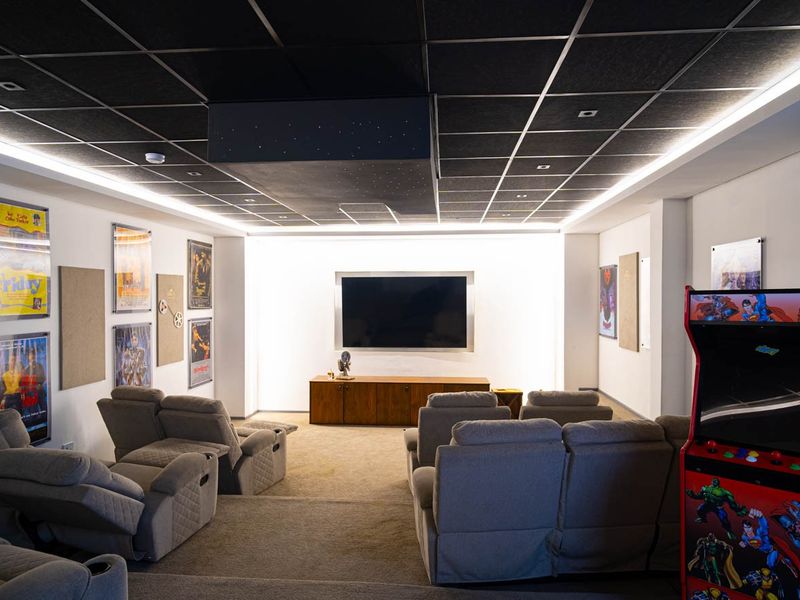 A professionally designed home cinema room featuring tiered seating, acoustic wall treatments, a dropped ceiling with ambient lighting, and a built-in media console.