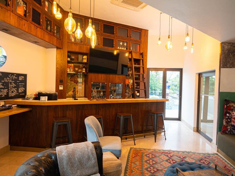 A well-appointed home bar featuring custom dark wood cabinetry, a built-in counter, library ladder, and stylish pendant lighting, opening onto an outdoor area.