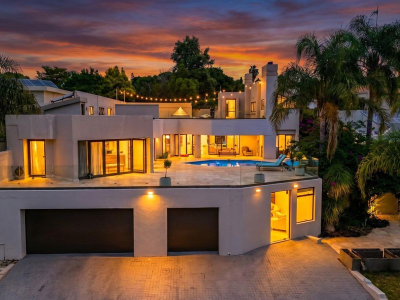 Stunning rear elevation featuring a spacious terrace, swimming pool, glass balustrades, and integrated double garage at twilight.