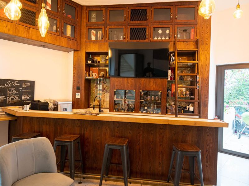 A well-appointed home bar featuring custom dark wood cabinetry, integrated shelving, a built-in sink, and a sliding ladder, with direct access to the pool area.