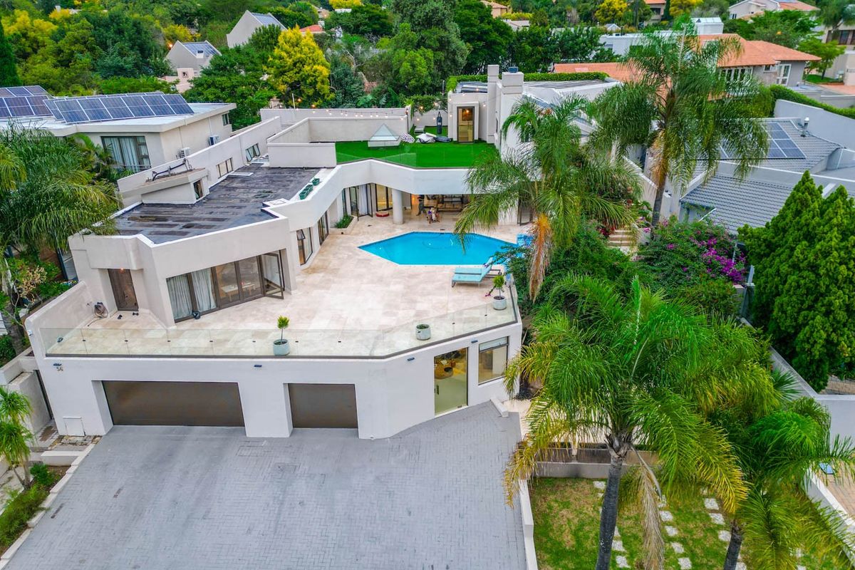 Aerial view of a modern multi-level residence featuring a swimming pool, spacious paved patio, roof terrace, and integrated double garage.