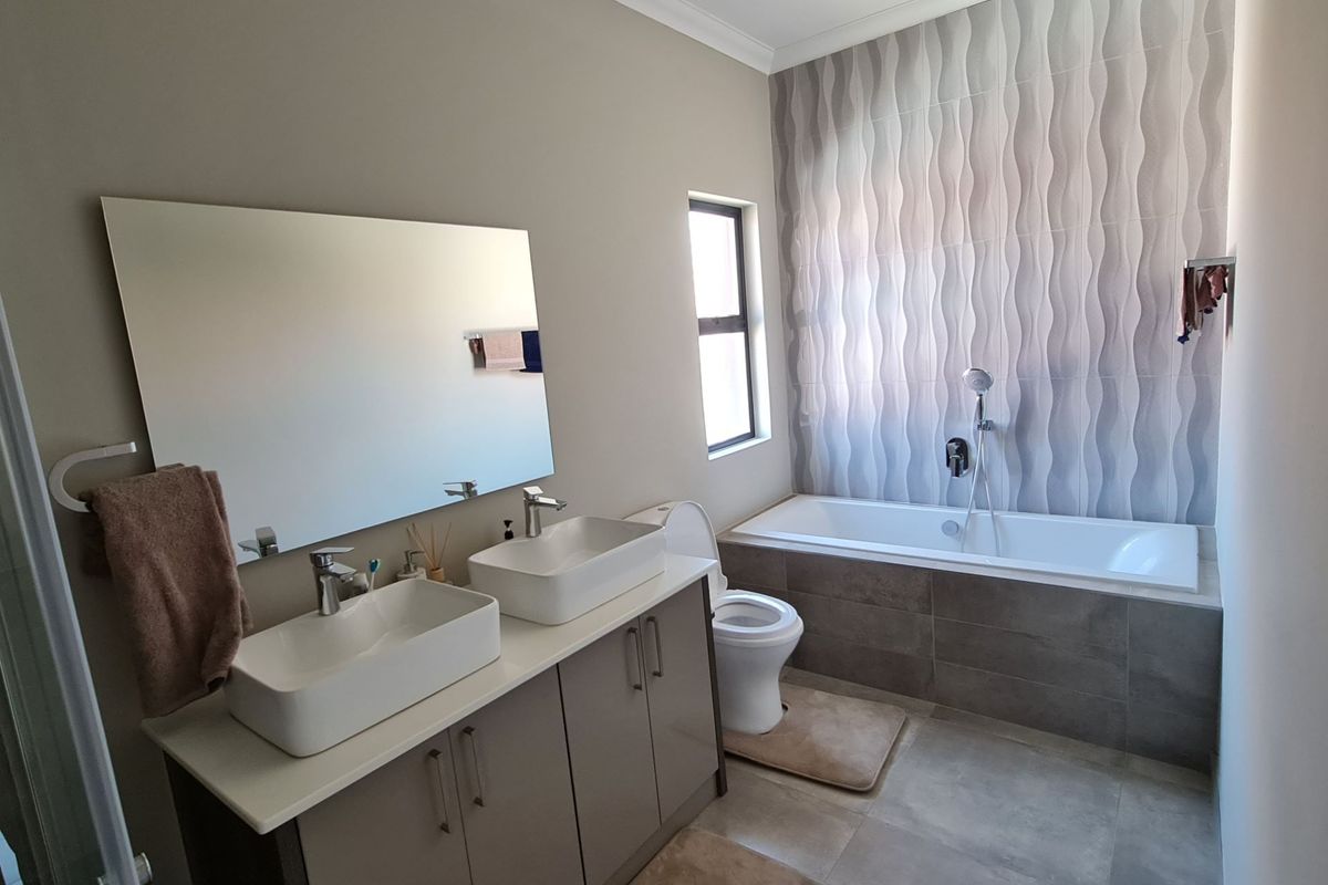 Modern bathroom featuring a double vanity with vessel sinks, a built-in bathtub with feature wall tiling, and neutral floor tiles.