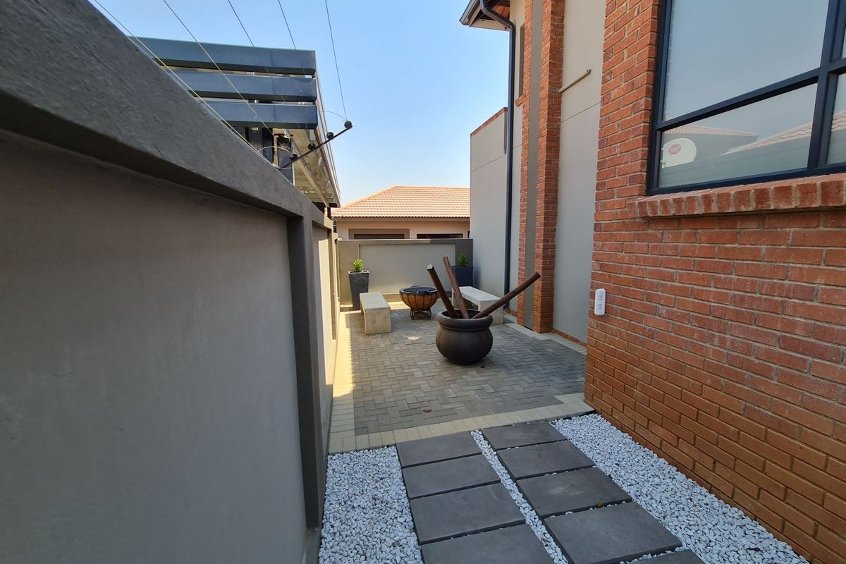 A neat rear courtyard featuring a paved patio area, stone pathway, and brick exterior wall finish.