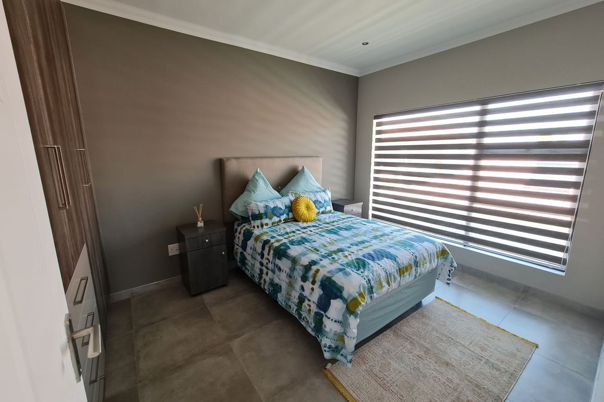 A well-maintained bedroom featuring neutral wall tones, large format floor tiles, built-in cabinetry, and modern zebra blinds for adjustable natural light.