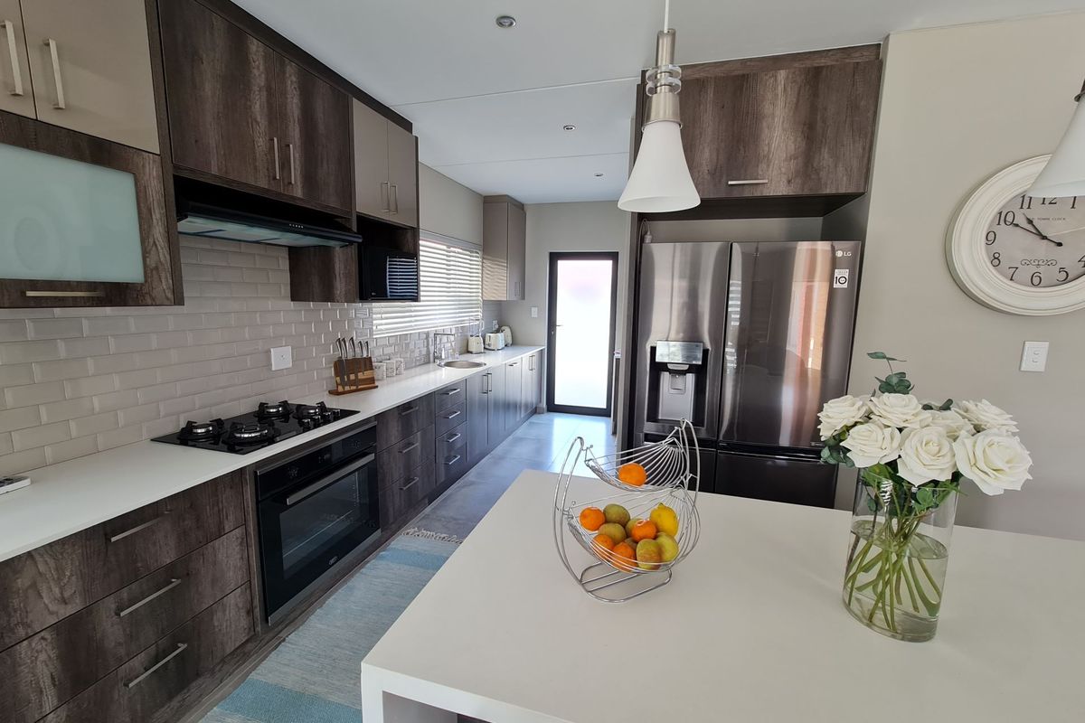 Modern kitchen featuring dark wood cabinetry, stone countertops, subway tile backsplash, gas hob, built-in oven, and a central island with pendant lighting.