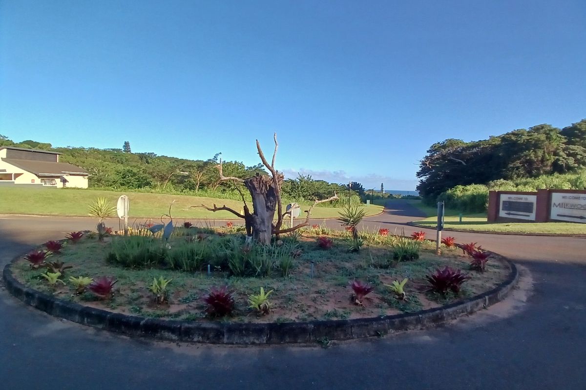 A view of a landscaped roundabout and entrance road within a residential estate, featuring established greenery and clear signage.