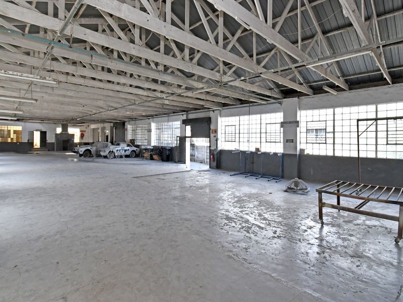 Spacious industrial workshop featuring exposed timber roof trusses, large steel-framed windows, and durable concrete flooring, suitable for various commercial or manufacturing operations.