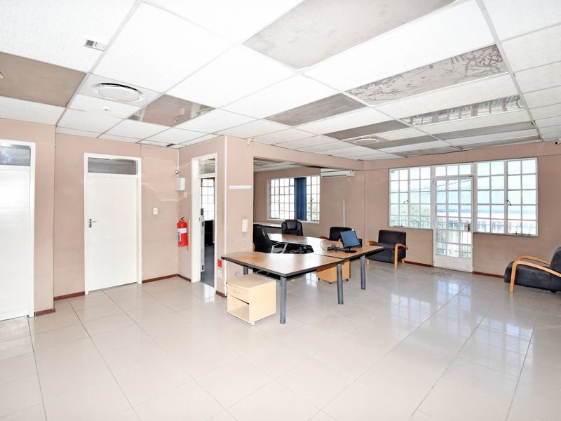 Spacious industrial office area featuring tiled flooring, suspended ceiling with integrated lighting, and large windows providing natural light.