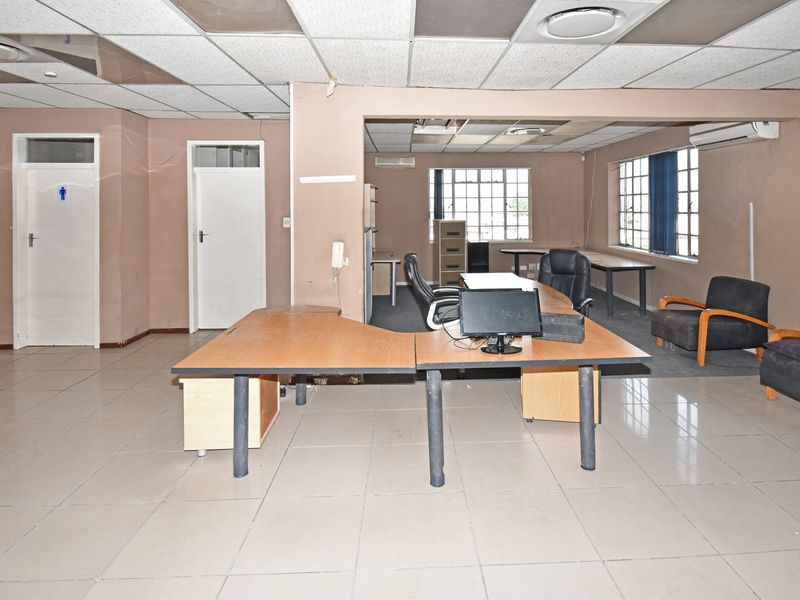 Open-plan industrial office space featuring tiled flooring, suspended ceiling tiles, and multiple windows providing natural light.