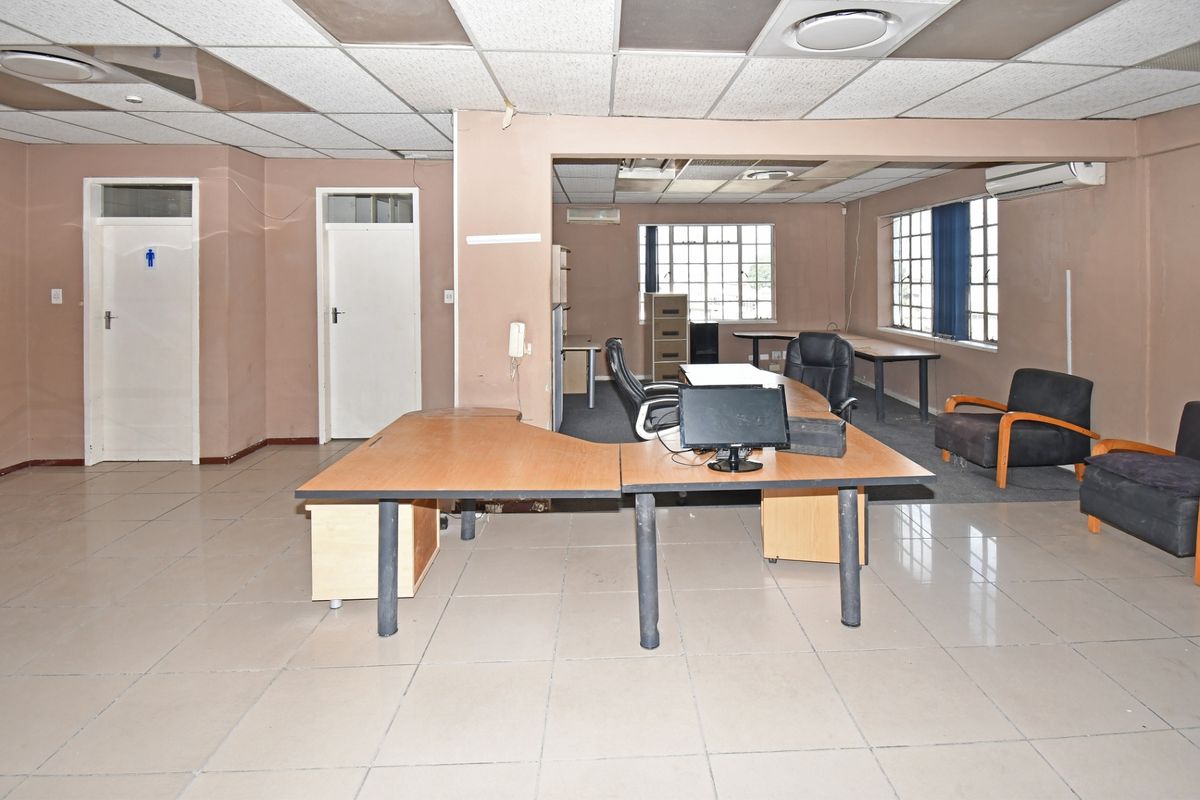 Open-plan industrial office space featuring tiled flooring, suspended ceiling tiles, and multiple windows providing natural light.