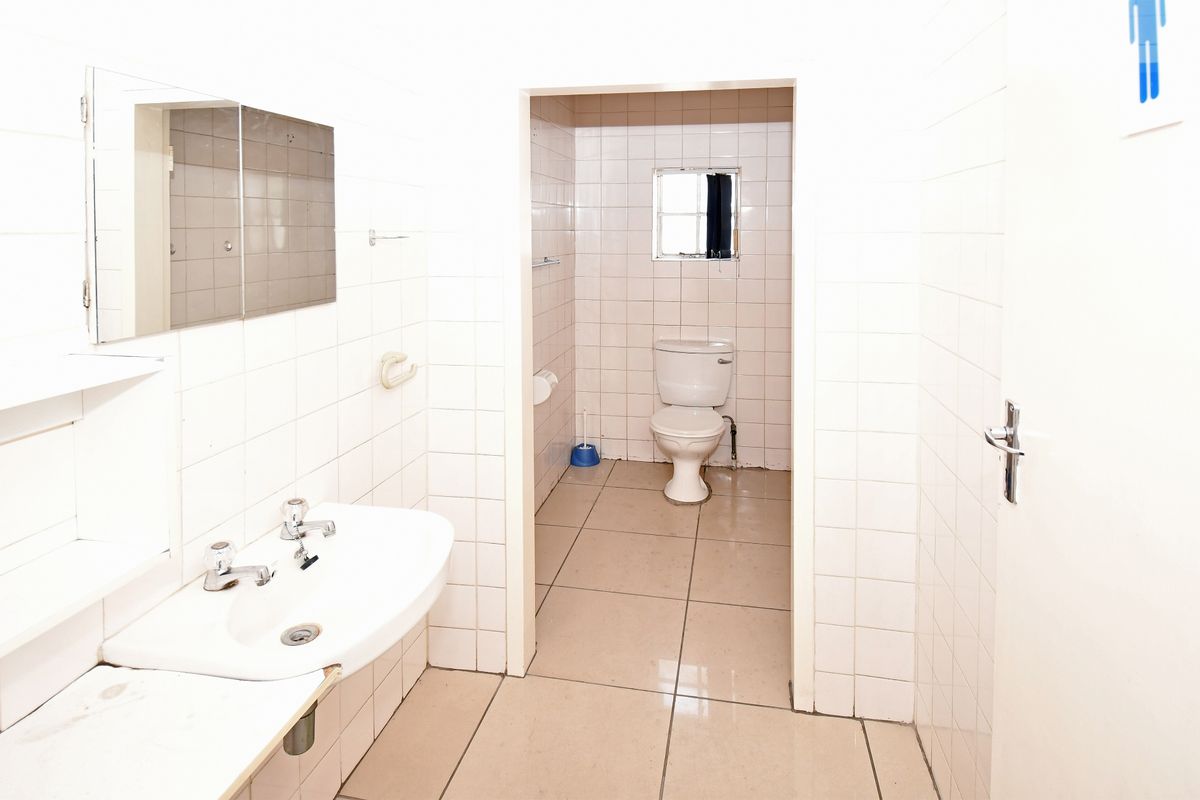 A functional industrial-style bathroom featuring white wall tiles, a pedestal basin, and a separate toilet area with tiled flooring.