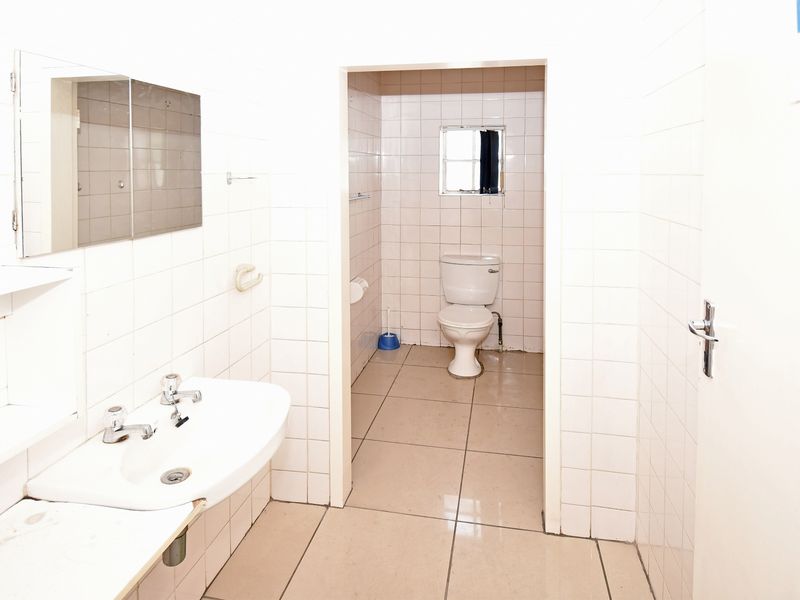 A functional industrial-style bathroom featuring white wall tiles, a pedestal basin, and a separate toilet area with tiled flooring.