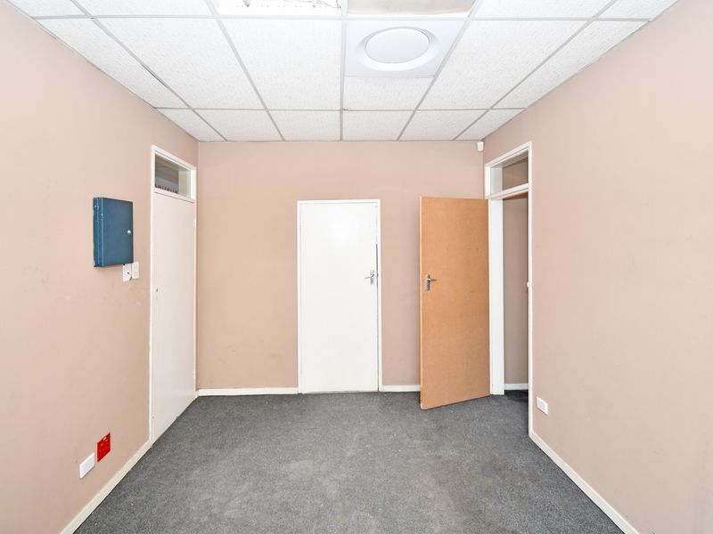 An empty office space featuring a suspended ceiling, carpeted flooring, and multiple internal access doors, suitable for a professional workspace.