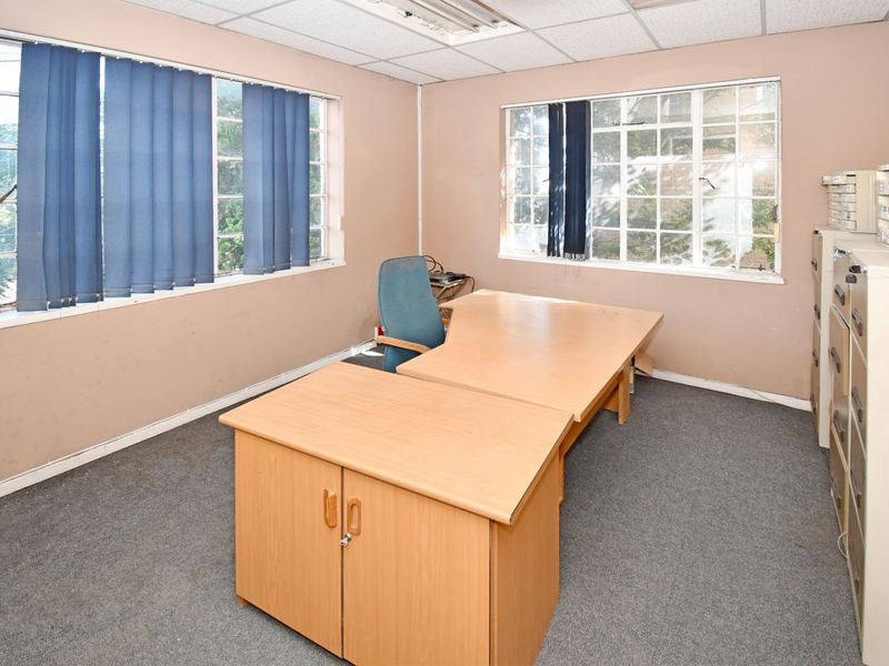A functional office space featuring carpeted flooring, suspended ceiling tiles, and large windows providing natural light.
