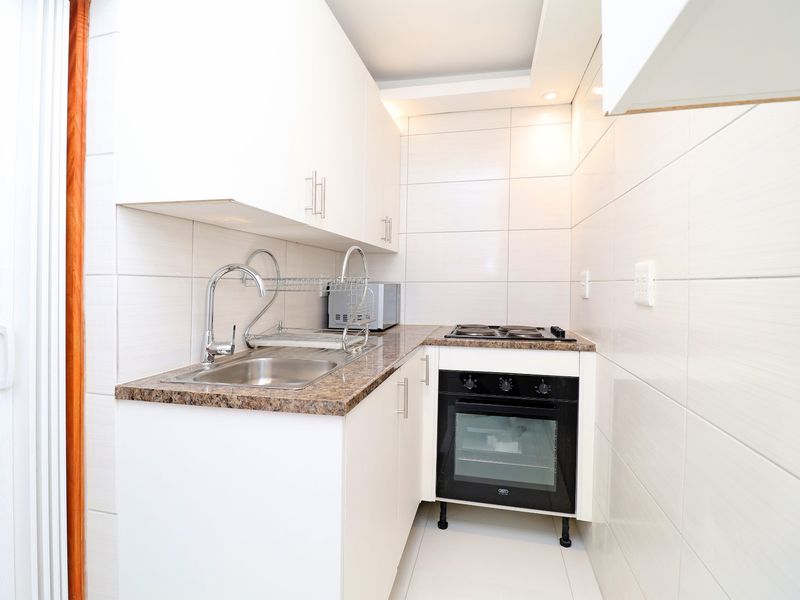 Compact modern kitchen featuring white cabinetry, granite countertops, a built-in oven, electric hob, and fully tiled finishes for a clean, functional workspace.