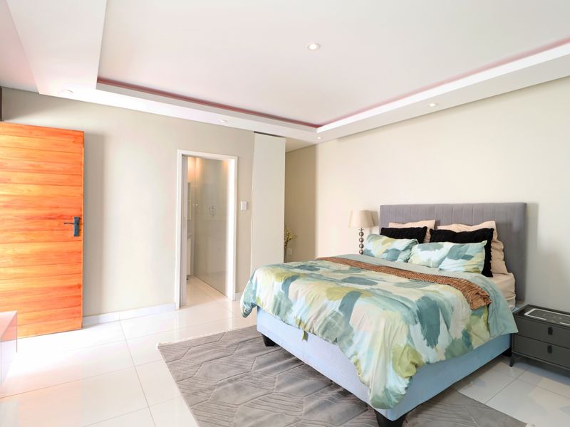 Spacious bedroom featuring modern tiled flooring, a recessed ceiling with integrated downlights, and direct access to an en-suite bathroom.