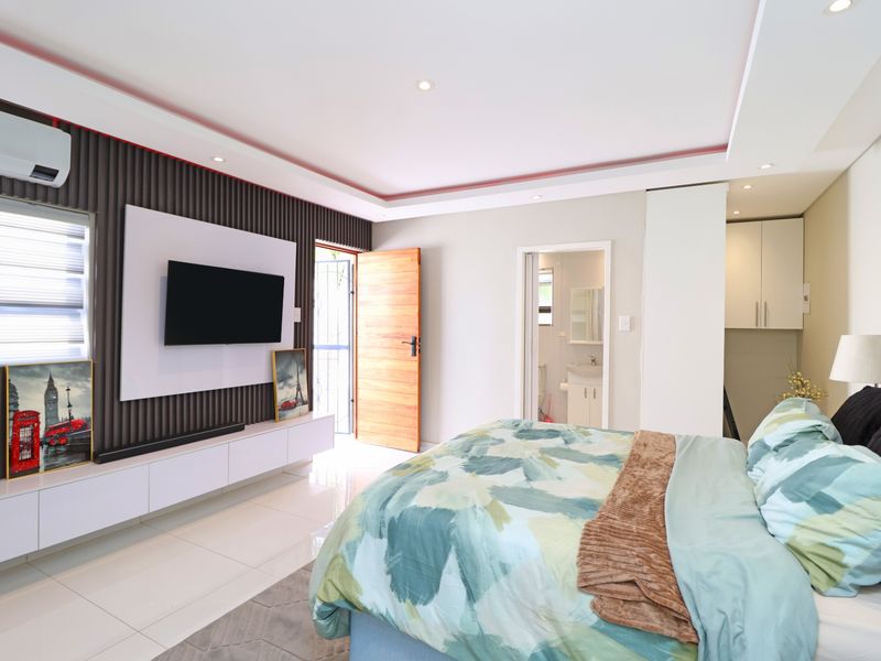 Modern bedroom featuring a slatted feature wall, built-in media console, recessed ceiling lighting, tiled floors, and an en-suite bathroom.